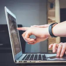 Person pointing at a laptop screen.