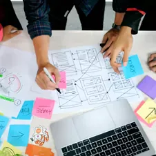 A group collaborating on a UX wireframe with sticky notes and sketches, symbolizing strategic planning and problem-solving.