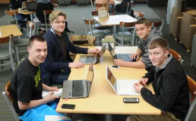 4 people sitting down at a table, each with their laptops.