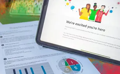 A tablet screen welcoming users to DISC, placed over printed assessment reports.