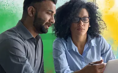 A man and woman reviewing information on a tablet in a workplace setting.