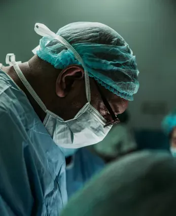 A focused surgeon in protective gear performing a procedure, symbolizing precision, care, and service.
