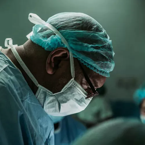 A focused surgeon in protective gear performing a procedure, symbolizing precision, care, and service.