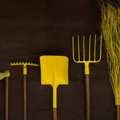 A row of yellow gardening tools against a dark wooden wall, representing preparation, efficiency, and the right tools for the job.