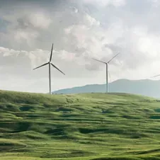 Wind turbines on rolling green hills under a cloudy sky, representing sustainable energy and optimized performance.